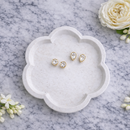 White jewelry dish with gold earrings on a marble surface with white flowers.