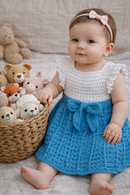Baby in a white top and blue skirt with a basket of teddy bears