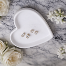 Heart-shaped white jewelry dish with earrings on a marble surface surrounded by white flowers.