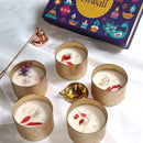 Decorative candles with flowers in gold holders on a white surface, with a Diwali-themed box in the background.